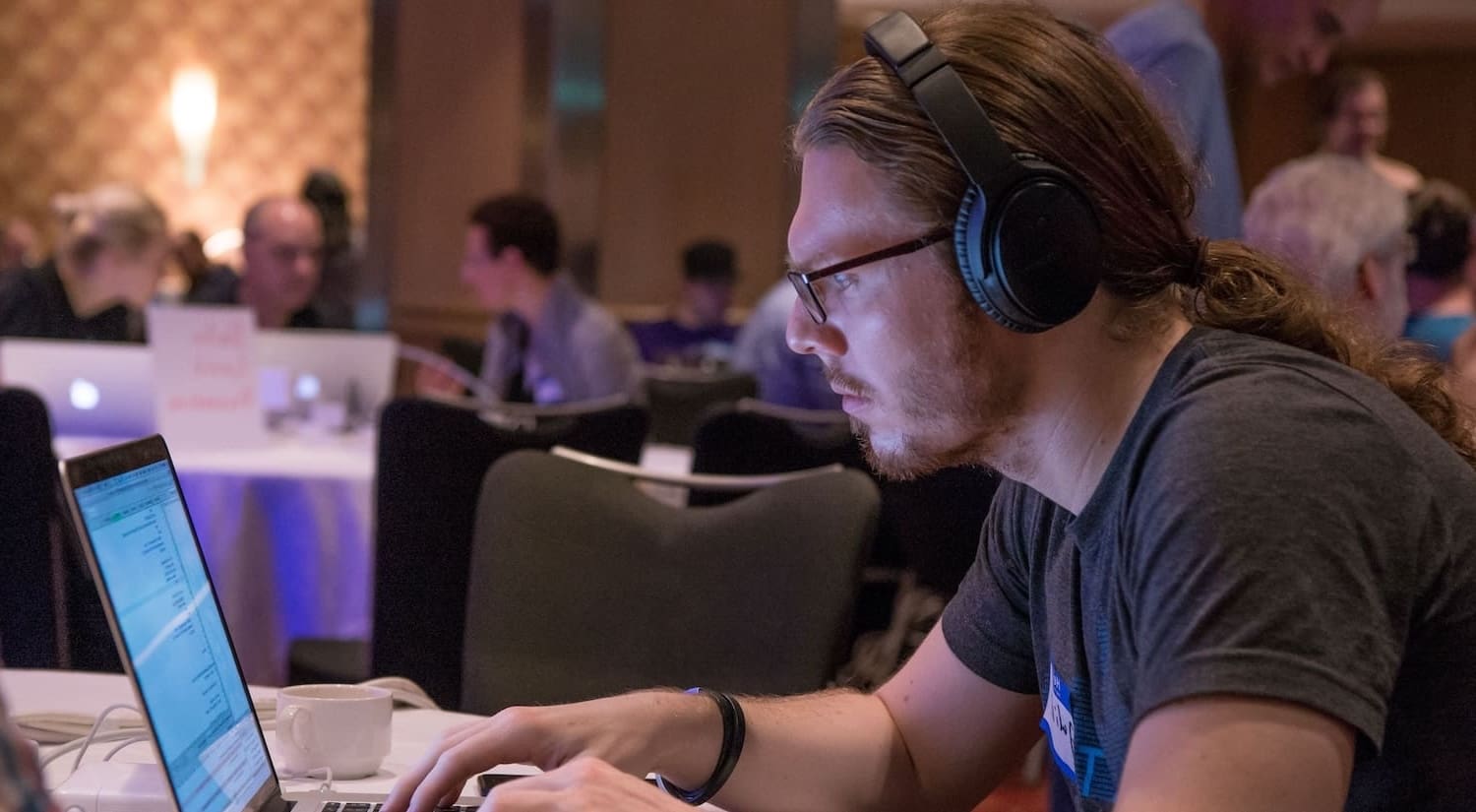 A man with headphones sits at a table, working on a laptop.