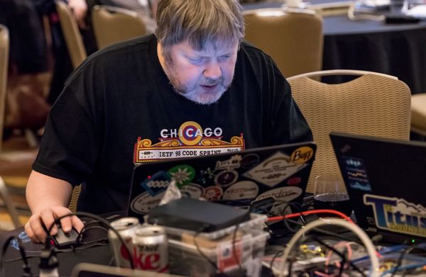 A man in a black shirt sits at a table, working on a laptop.