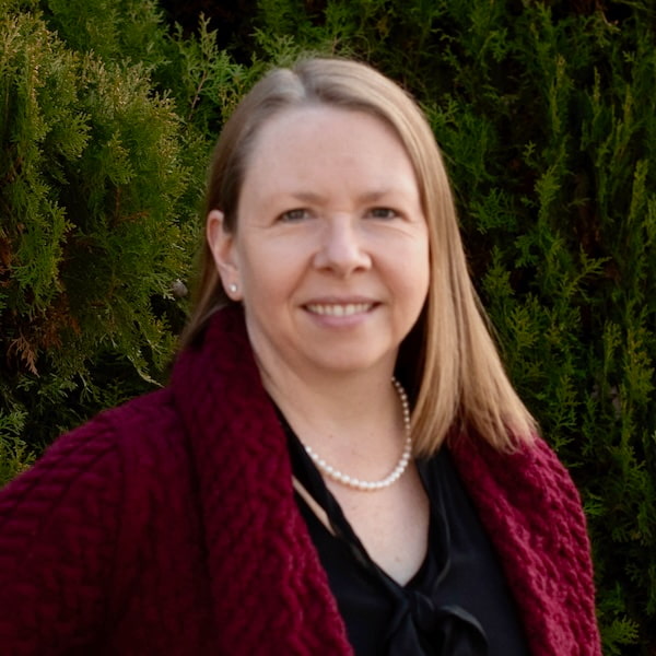 a woman in red sweater with trees behind her