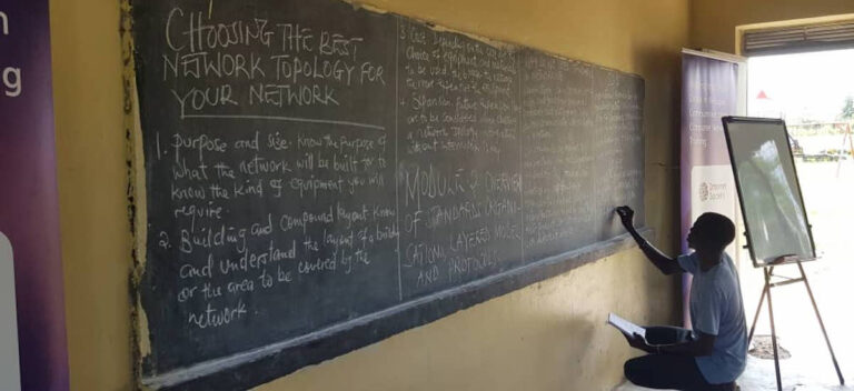 A man kneels and writes on a large chalkboard