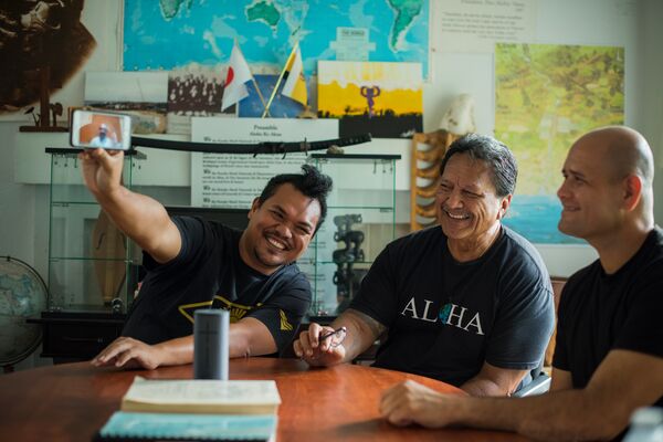 Three men sitting at a table, smiling and watching a video together