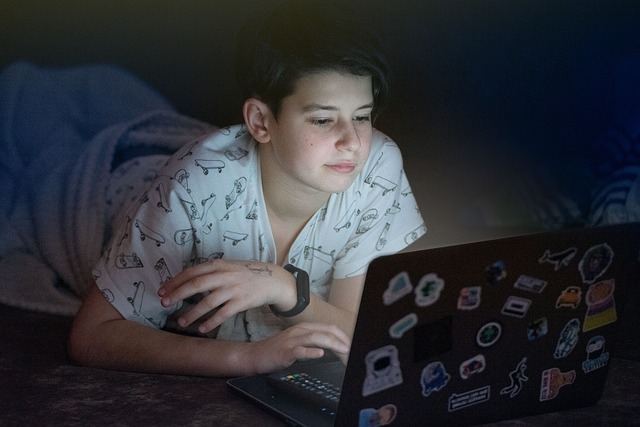 A young man reclines on his bed, using a laptop
