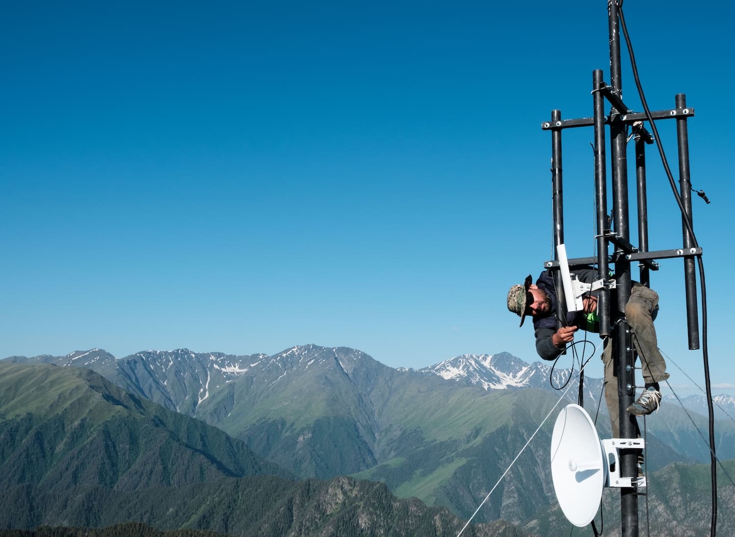 A man adjusts a satellite dish on a mountain peak