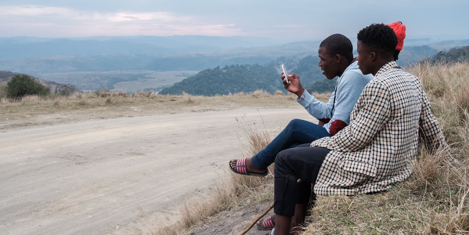 people sitting on a hillside, focused on a cell phone