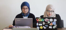 Two women sit side by side behind their laptops