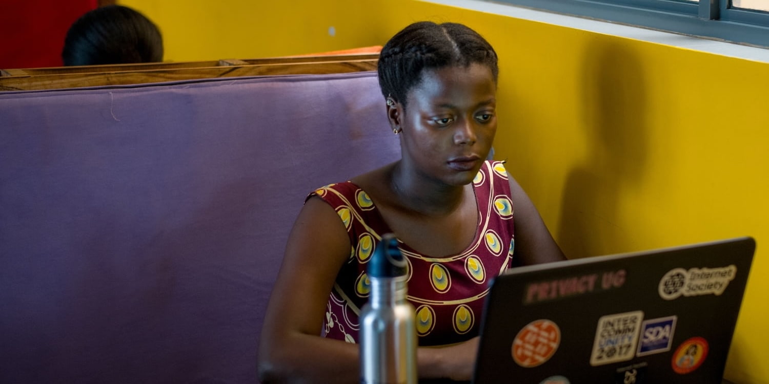 A woman seated at a table, focused on her laptop while working or studying.