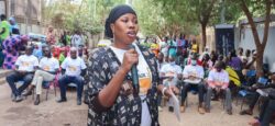 A woman stands and speaks into a microphone at a Mali Chapter event
