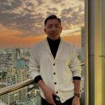 A man standing on a balcony holding a mobile phone in its hand