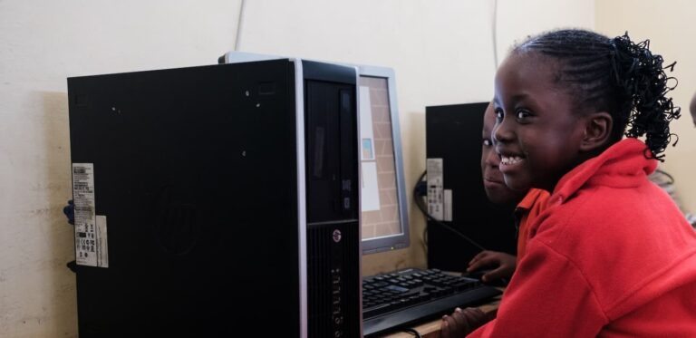 A young girl smiles while happily using a computer