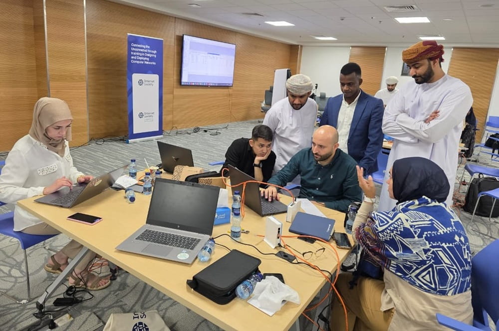 Personas de pie alrededor de un escritorio mirando sus computadoras portátiles