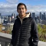 A man in a black jacket stands leaning on a rampart