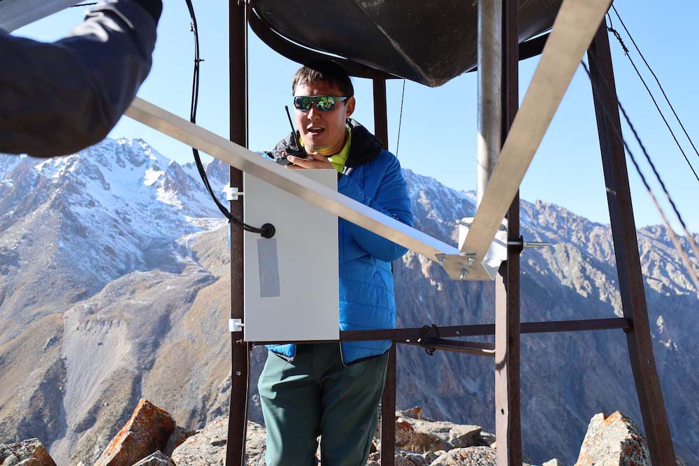 A man stands in mountainous terrain next to connectivity infrastructure