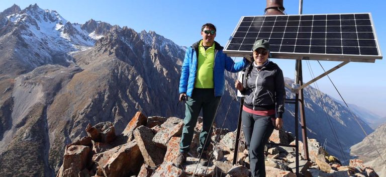 Two people stand in mountainous terrain next to connectivity infrastructure