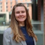 A woman in a grey blazer jacket and dark blue shirt, smiling