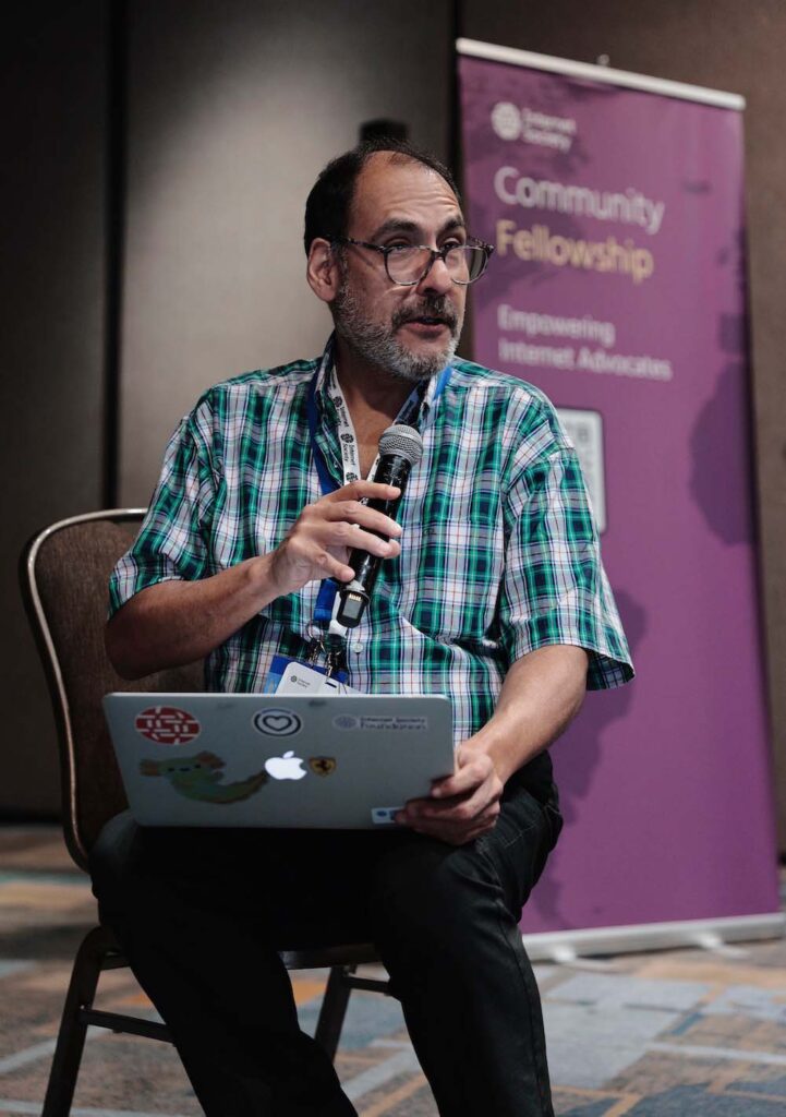 A man sits and speaks into a microphone at a community workshop