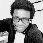 A black and white photo of a man in white T-shirt and black hoodie, wearing glasses