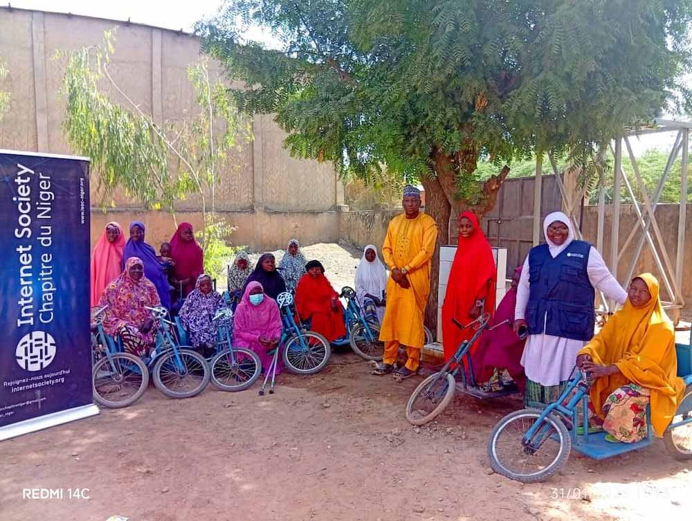 A group of people, many with bikes, stand and sit outside next to an Internet Society Niger Chapter sign