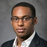 A man with glasses wearing a white shirt and black suit