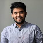 A man is a light grey shirt smiling.