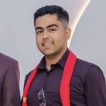 A man in a dark purple shirt wearing a red stripe aground the neck.