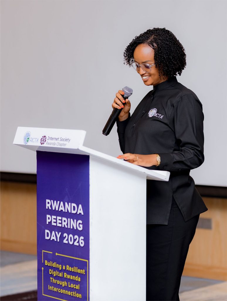 A woman stands at a podium and holds a microphone at Rwanda Peering Day