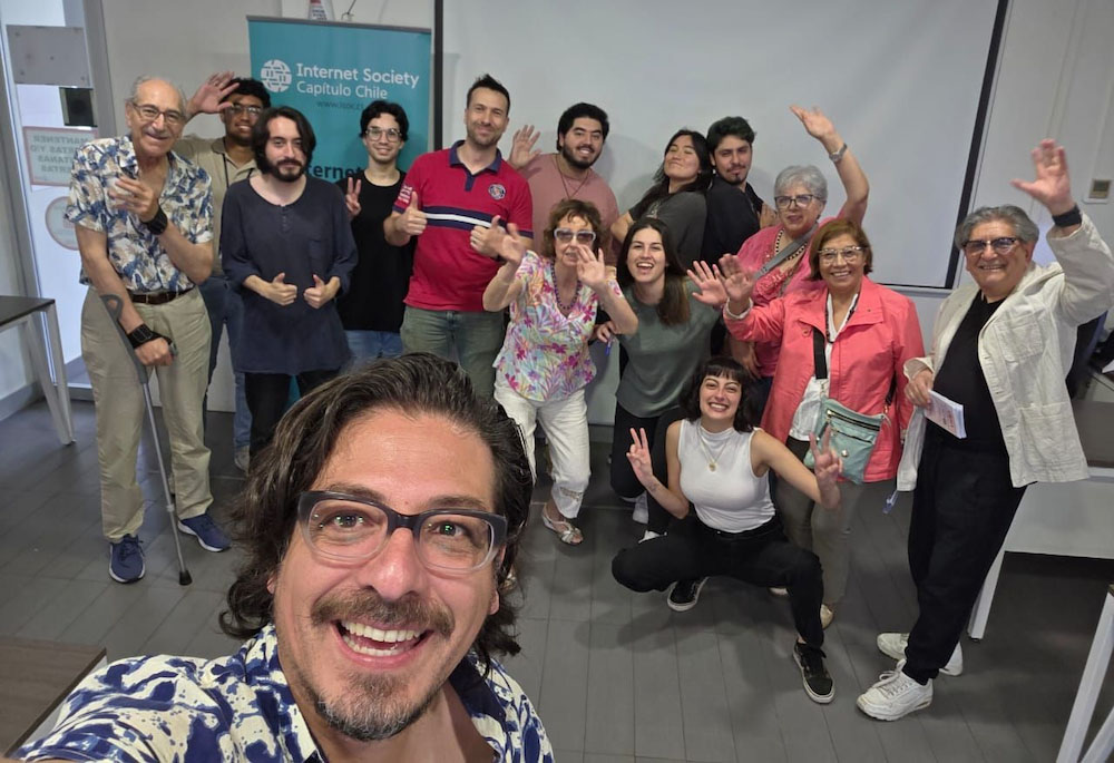 A man takes a selfie with a group of people standing behind him. 