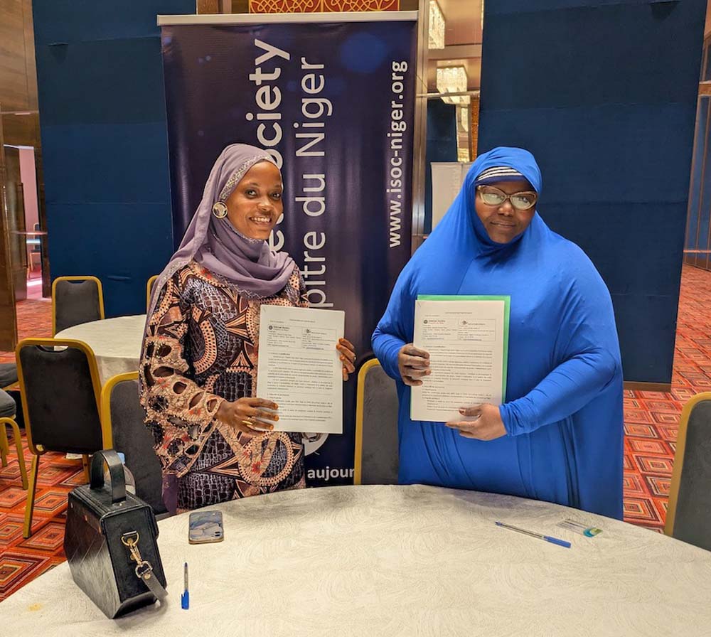 Two woman stand together and hold documents in front of an Internet Society Niger Chapter sign