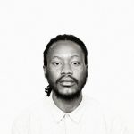 A black and white portrait of a man with dreadlocks