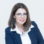 A woman wearing glasses, a white shirt, and a blue jacket