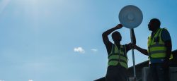 Two men in yellow vests mount a network antenna on a roof.