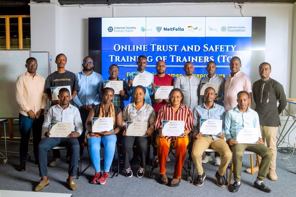 A group of seated and standing people hold certificates and pose together in front of an Internet Society Rwanda Chapter sign.