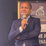 A man in a suit stands confidently, holding a microphone