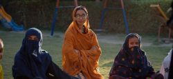 Three women sit on the grass outside