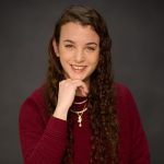 A young woman with long curly hair wearing a red sweater