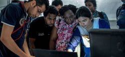 A group of people gather around a computer