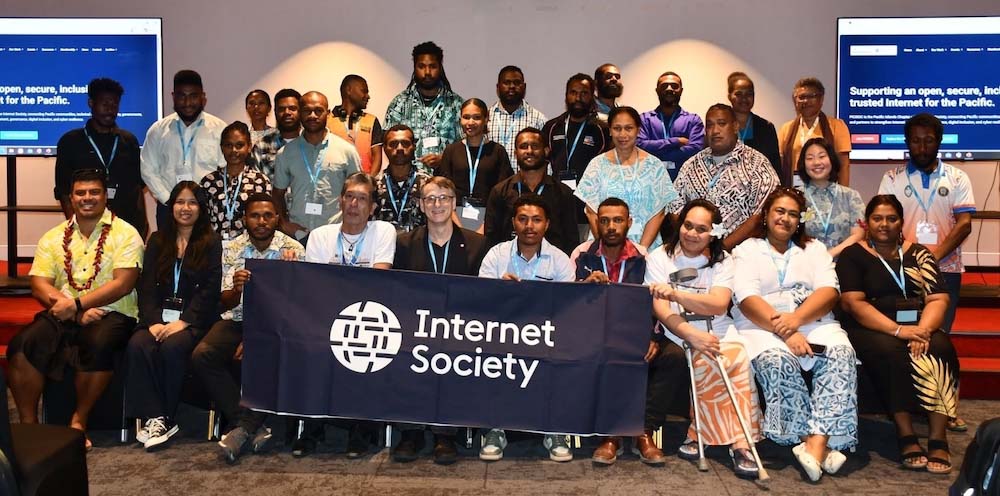 A large group of people get together and hold an Internet Society sign.