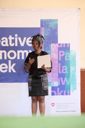 A woman stands in front of a banner reading ''Banner for Creative Economy Week''