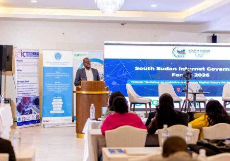 A man stands at a podium and speaks to a seated audience. A sign behind him says South Sudan Internet Governance Forum.