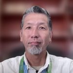 A man with a white beard wearing a green tie about the neck.